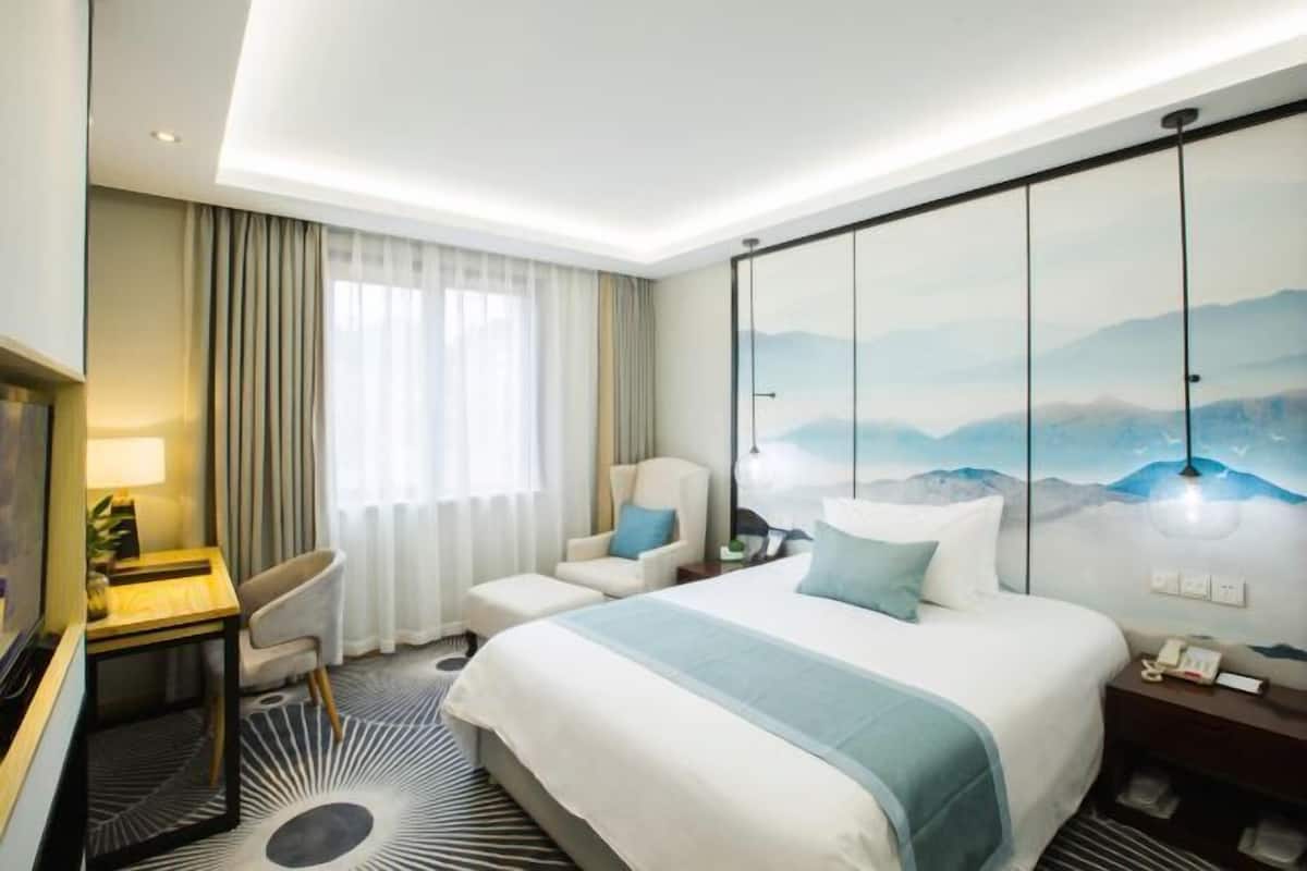 Habitación de hotel con cama, escritorio, silla, televisor y un cuadro en la pared.
