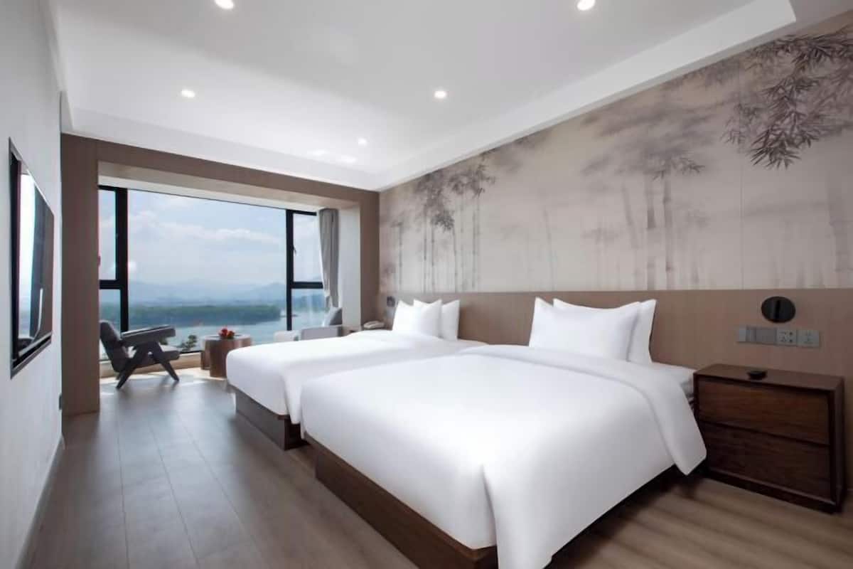 Habitación de hotel con dos camas, un ventanal con vistas, un cuadro en la pared y una mesita de noche.