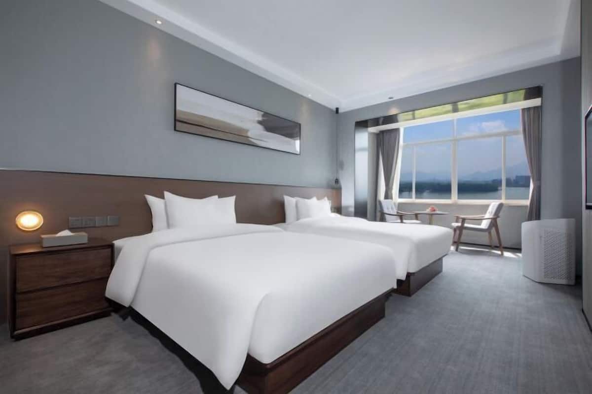 Habitación de hotel moderna con dos camas, un ventanal con vistas, una mesita y una silla.