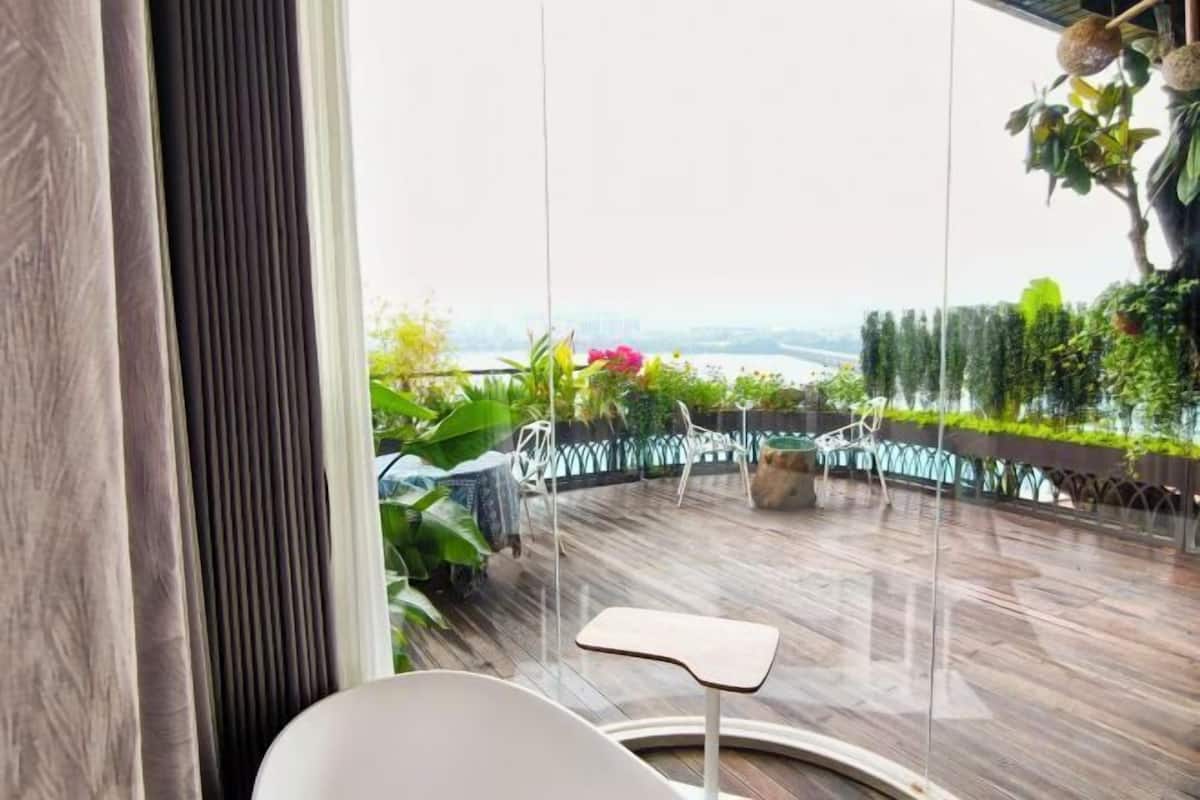 Una habitación moderna con un gran ventanal, una silla blanca y vistas a zonas verdes y un cuerpo de agua.