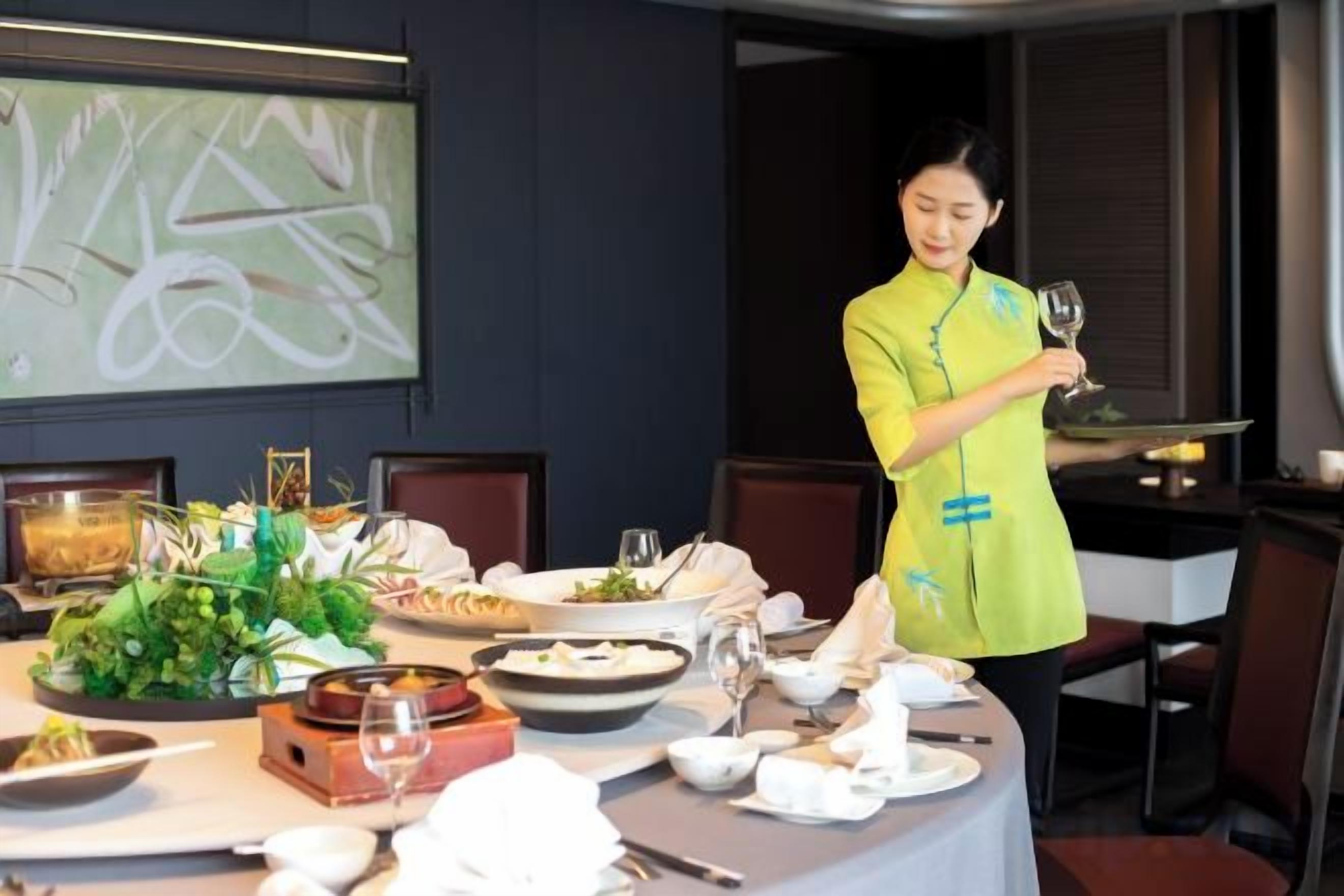 A dining table set with plates, glasses, and a centerpiece. A person in a yellow uniform is standing by the table.