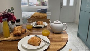 A breakfast setting with pastries, a teapot, and a glass of orange juice on a wooden table.