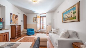 A living room with a sofa, ottoman, and a blue chair. There is a painting on the wall and a wooden cabinet. - Ostuni's Corner by Rentbeat (Ostuni)