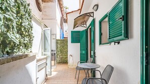 A narrow outdoor corridor with a tiled floor, a small round table with chairs, and green shutters on the windows. - Ostuni's Corner by Rentbeat (Ostuni)