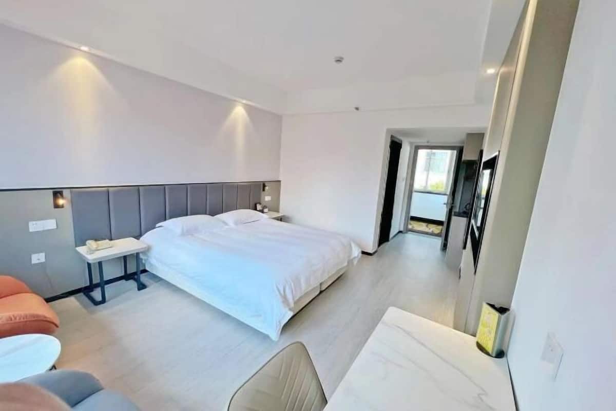 A modern hotel room with a large bed, a bedside table, a chair, and a small table.