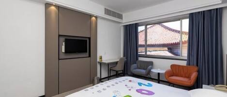 A modern hotel room with a bed, a TV, a desk, and a view of traditional architecture.