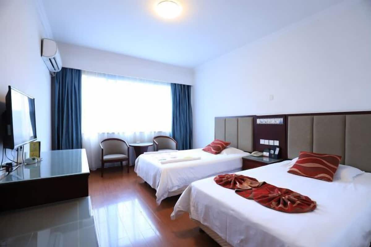 A hotel room with two beds, a desk, a chair, a television, and a window with curtains.