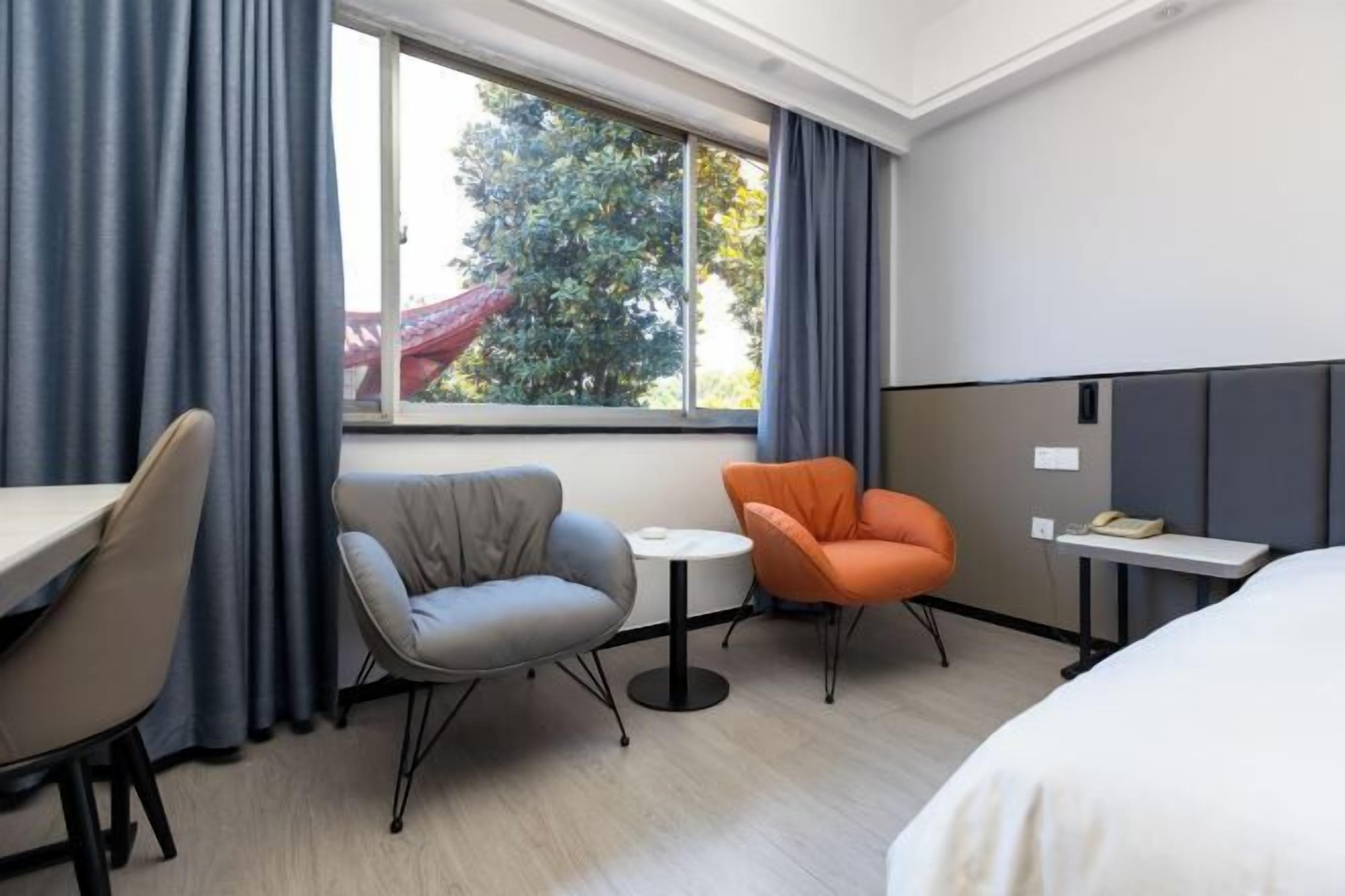 A hotel room with a bed, a desk, two chairs, a small table, and a window with curtains.