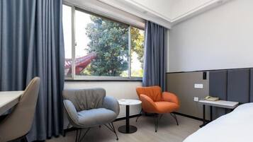 A hotel room with a bed, a desk, two chairs, a small table, and a window with curtains.