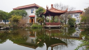 A traditional Chinese pavilion over a pond, surrounded by trees and buildings. - Hengdian World Studios Resort (Dongyang)