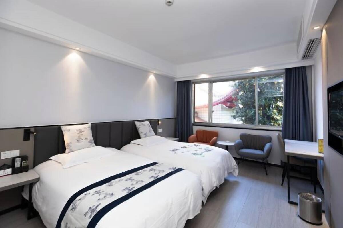 A hotel room with two beds, a desk, a chair, a TV, and a window with a view.