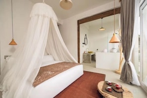 A bedroom with a canopy bed, a bedside table with candles, and a view of the bathroom through an open door.