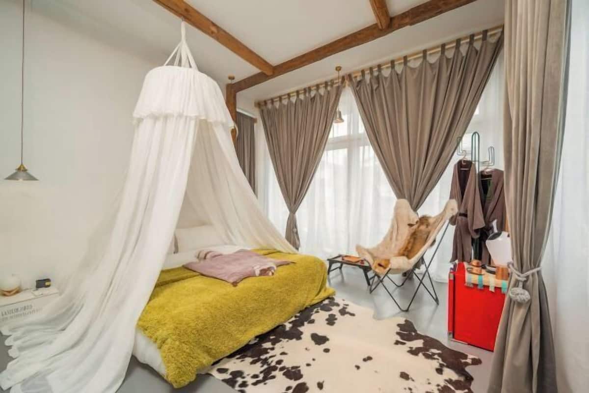 Ein Schlafzimmer mit Himmelbett, einem Sessel, einem roten Schrank und einem Kuhfellteppich.