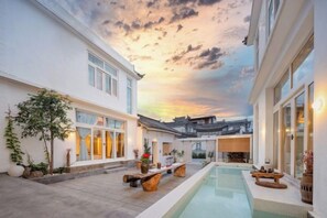 A modern building with a pool, traditional architecture, and a sunset sky.
