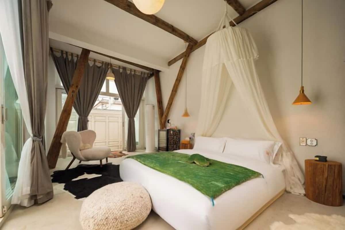 Ein Schlafzimmer mit einem Bett, einem Sessel, einem Nachttisch und einer Pendelleuchte.