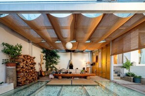 A modern interior with a glass pool, wooden ceiling, and various plants.