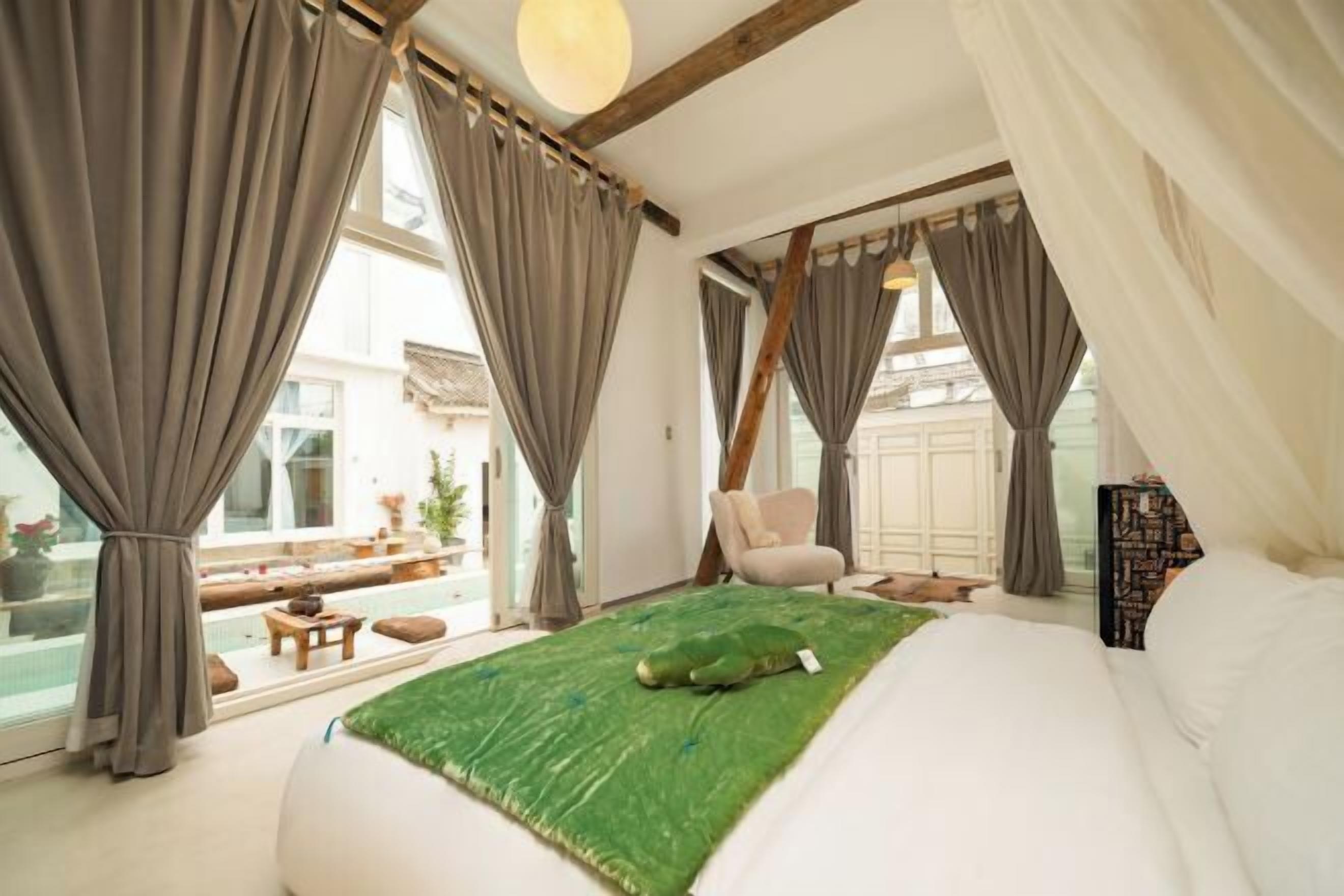 A bedroom with a large bed, a green area rug, a chair, and a view of a balcony with outdoor furniture.