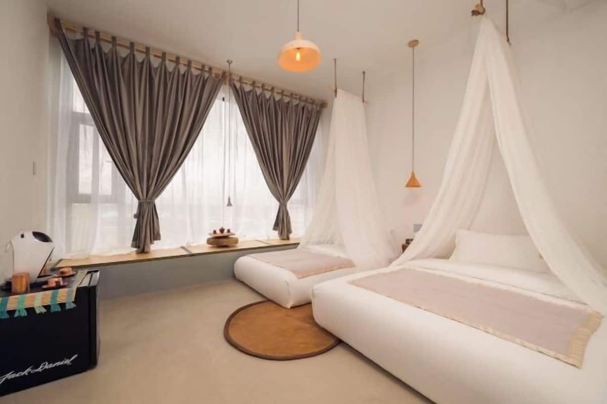 Ein Schlafzimmer mit zwei Betten, einem Fenster mit Vorhängen, einem Nachttisch und einer Lampe.
