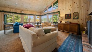A cozy room with a wooden ceiling, large windows, a fireplace, and a dining area with a table and chairs. - Lakefront Escape, On Snowmobile Trail, Near Town (Old Forge)