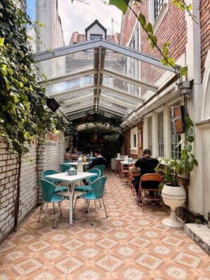 A covered outdoor seating area with tables and chairs, brick walls, and a tiled floor. - Marietta - House of Social Travellers (Bogotá)