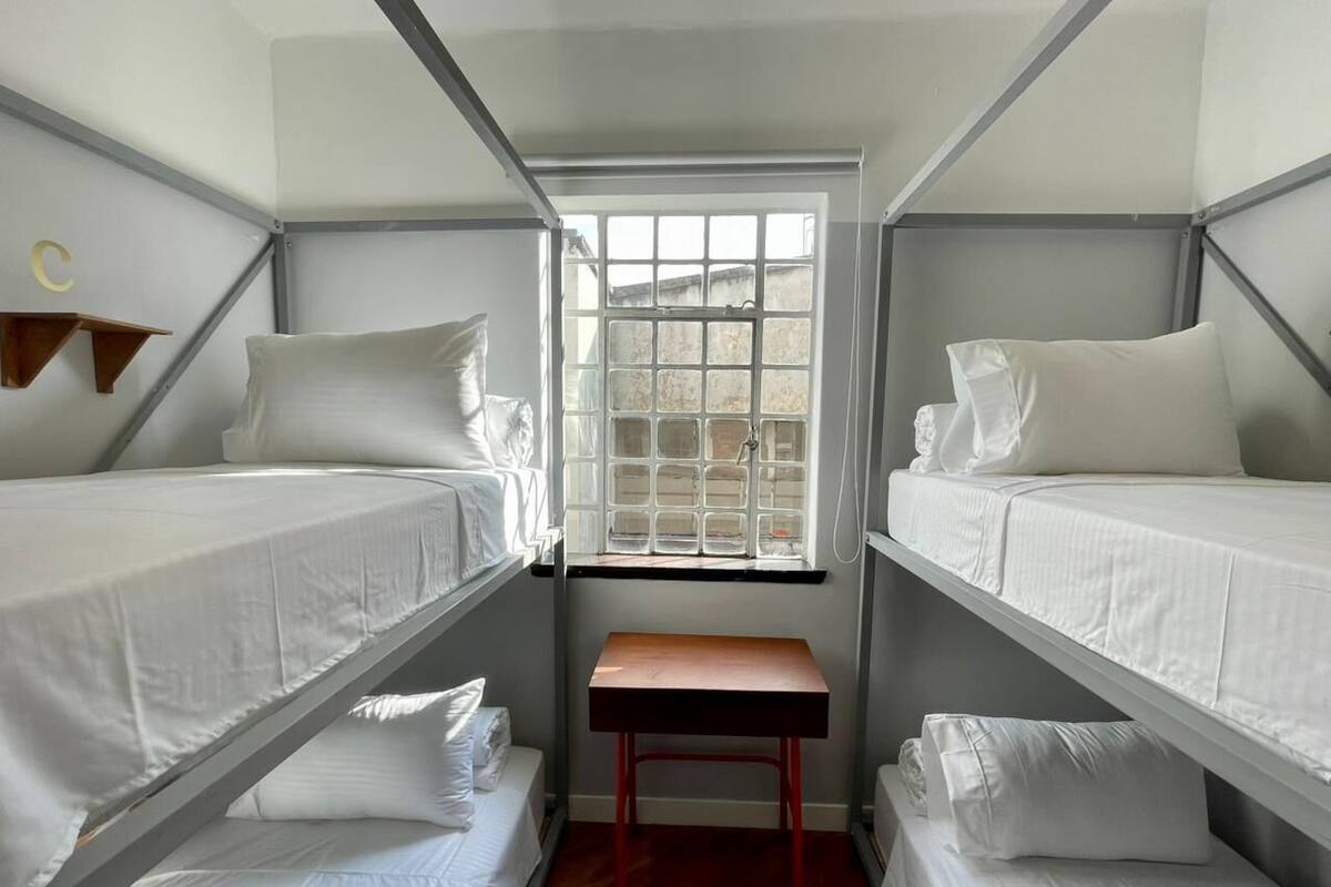 A dormitory room with bunk beds, a small table, and a window.