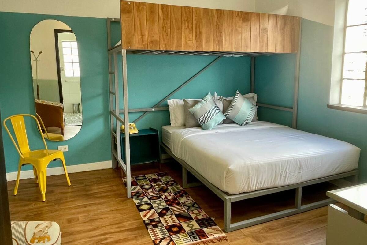 A bedroom with a bunk bed, a chair, a mirror, and a patterned rug.