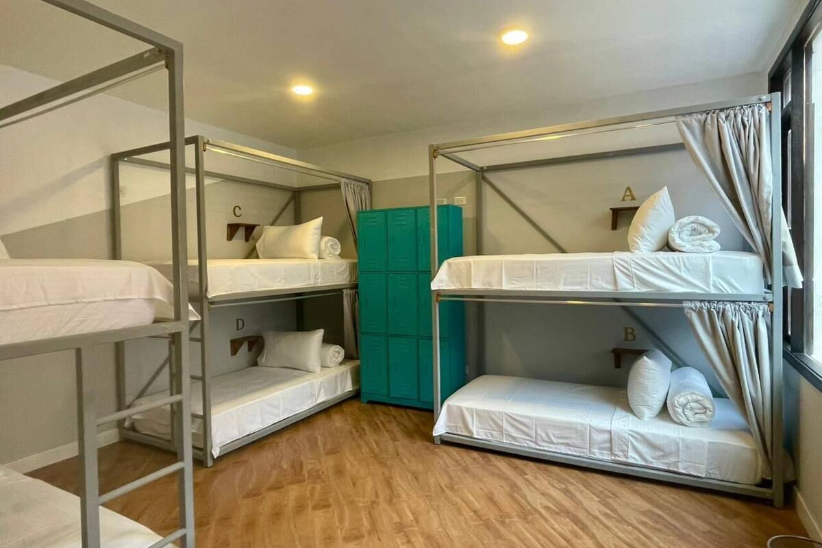 A bunk room with four bunk beds, a teal storage unit, and a wooden floor.