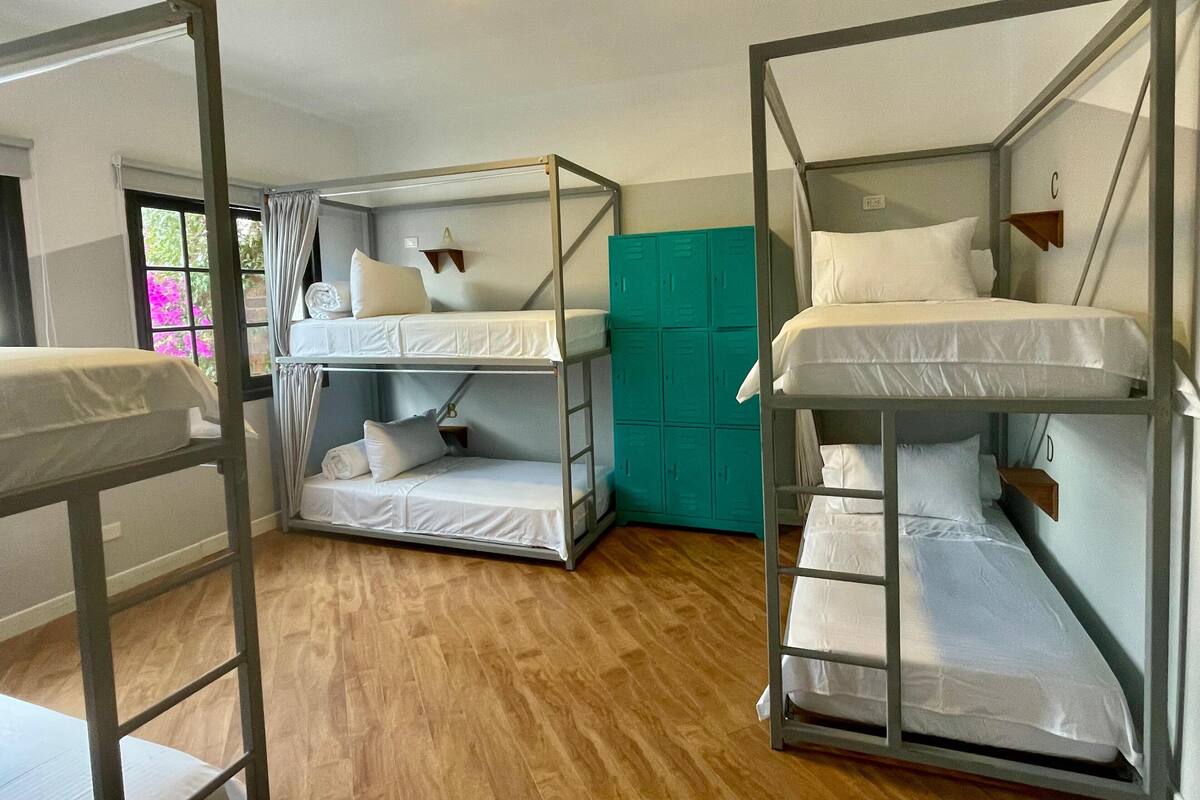 A room with bunk beds, a teal-colored wardrobe, and a window with curtains.