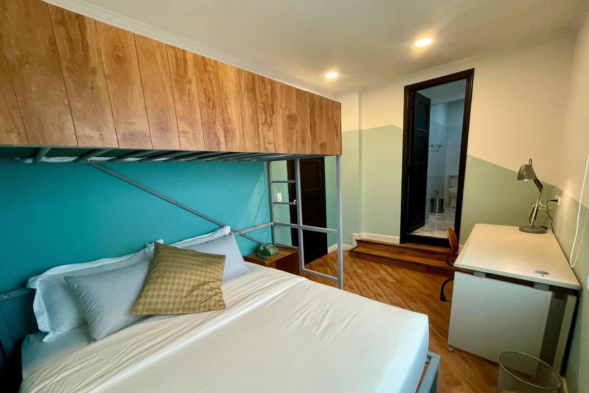 A bunk bed with a desk and chair, a small trash bin, and a mirror.