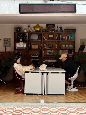 Ein Zimmer mit Schreibtisch, zwei Stühlen, einem Bücherregal und einer Heizung.