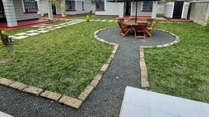 Un quartier résidentiel composé de plusieurs maisons, avec une pelouse centrale agrémentée d’une table et de chaises, et un chemin pavé.