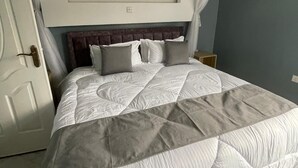 Une chambre à coucher avec un grand lit, une tête de lit sombre et un baldaquin blanc.