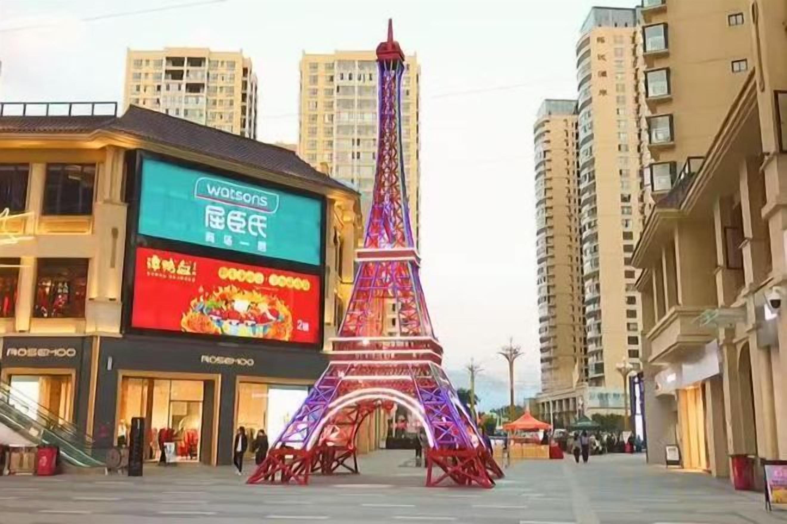 A building with a large illuminated sign, a replica of the Eiffel Tower, and high-rise residential buildings in the background.