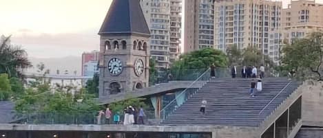 Una torre del reloj con techo puntiagudo, un puente peatonal y edificios altos al fondo.
