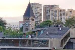 Een klokkentoren met een puntige top, een voetgangersbrug en hoge gebouwen op de achtergrond.