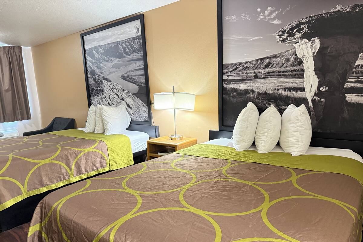 Une chambre d’hôtel avec deux lits, une table de chevet, une lampe et deux grandes affiches représentant des paysages accrochées au mur.