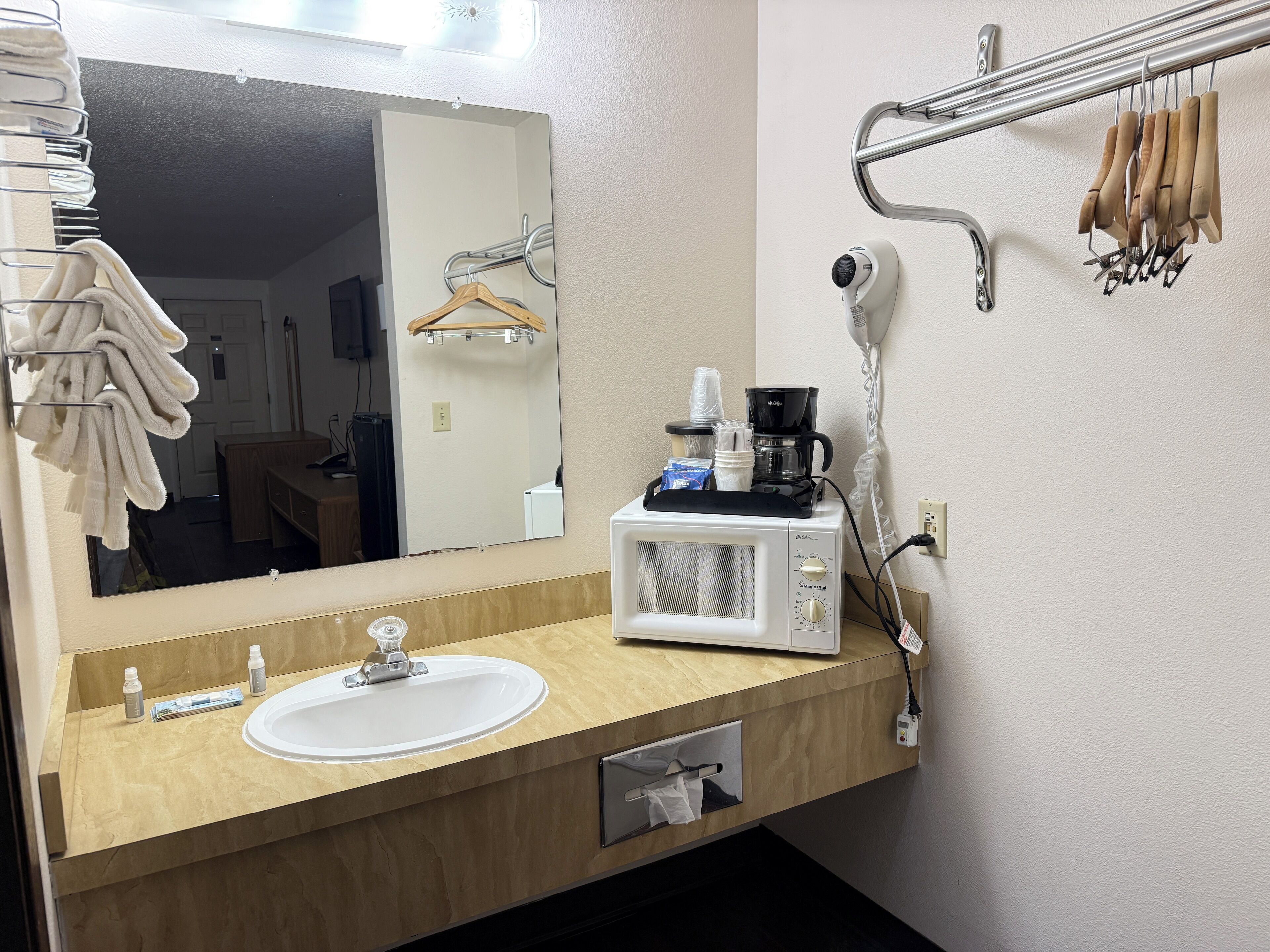 A bathroom with a sink, mirror, towel rack, and a coffee maker.