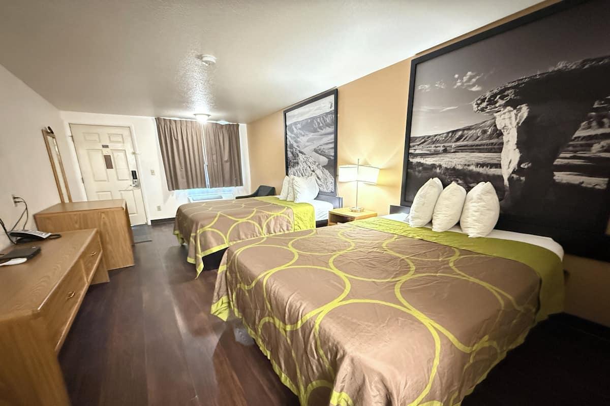 Une chambre d’hôtel avec deux lits, un bureau, une chaise et un grand tableau encadré au mur.