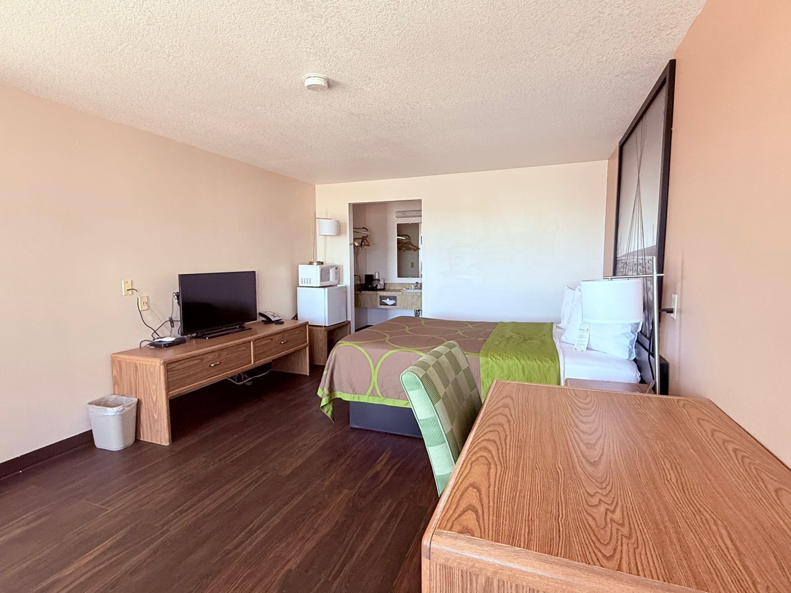 A hotel room with a bed, a desk with a television, a microwave, and a small trash bin.