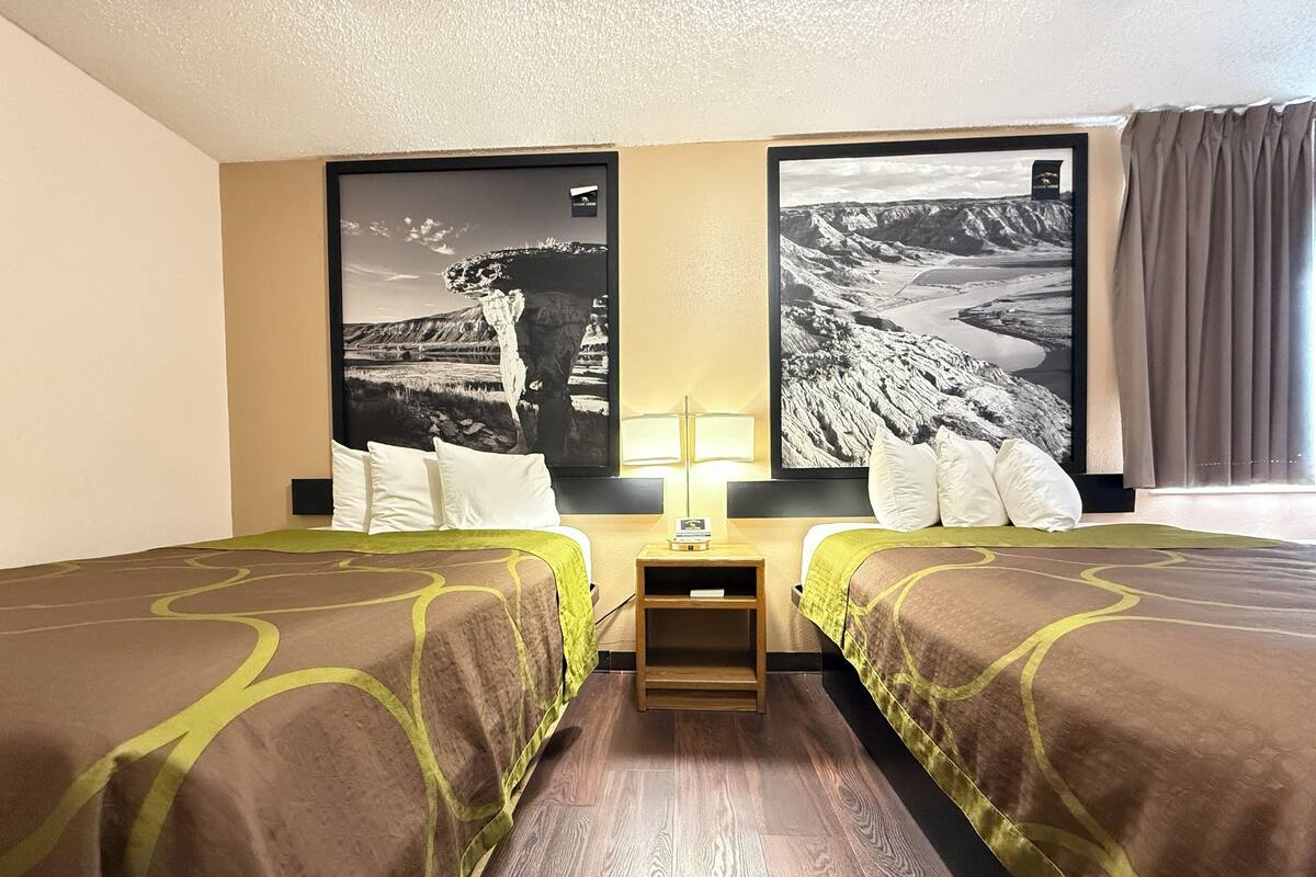 Une chambre d’hôtel avec deux lits, une table de chevet et deux grandes photographies encadrées accrochées aux murs.