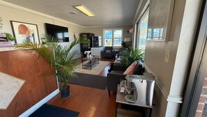 Ein modernes Wohnzimmer mit einem Holzbüro, einer Kaffeemaschine und einer Sitzecke mit Sofa und Sesseln.
