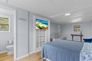 Un dormitorio con cama, ventana, puerta y televisor montado en la pared.