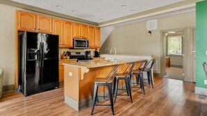 A kitchen with wooden cabinets, a black refrigerator, a microwave, and a bar area with stools.