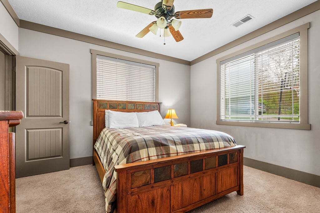 A bedroom with a wooden bed, a ceiling fan, a window with blinds, and a door.