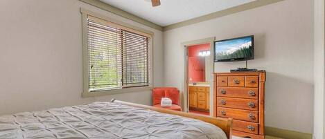 A bedroom with a bed, a ceiling fan, a dresser, a television, and a window with blinds.