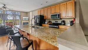 A kitchen with granite countertops, wooden cabinets, a refrigerator, a microwave, and a coffee maker.