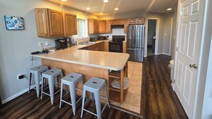 A kitchen with wooden cabinets, a central island with stools, a refrigerator, and a microwave. - Family Mountain Escape w/ Hot Tub & Game Room (Oakland)