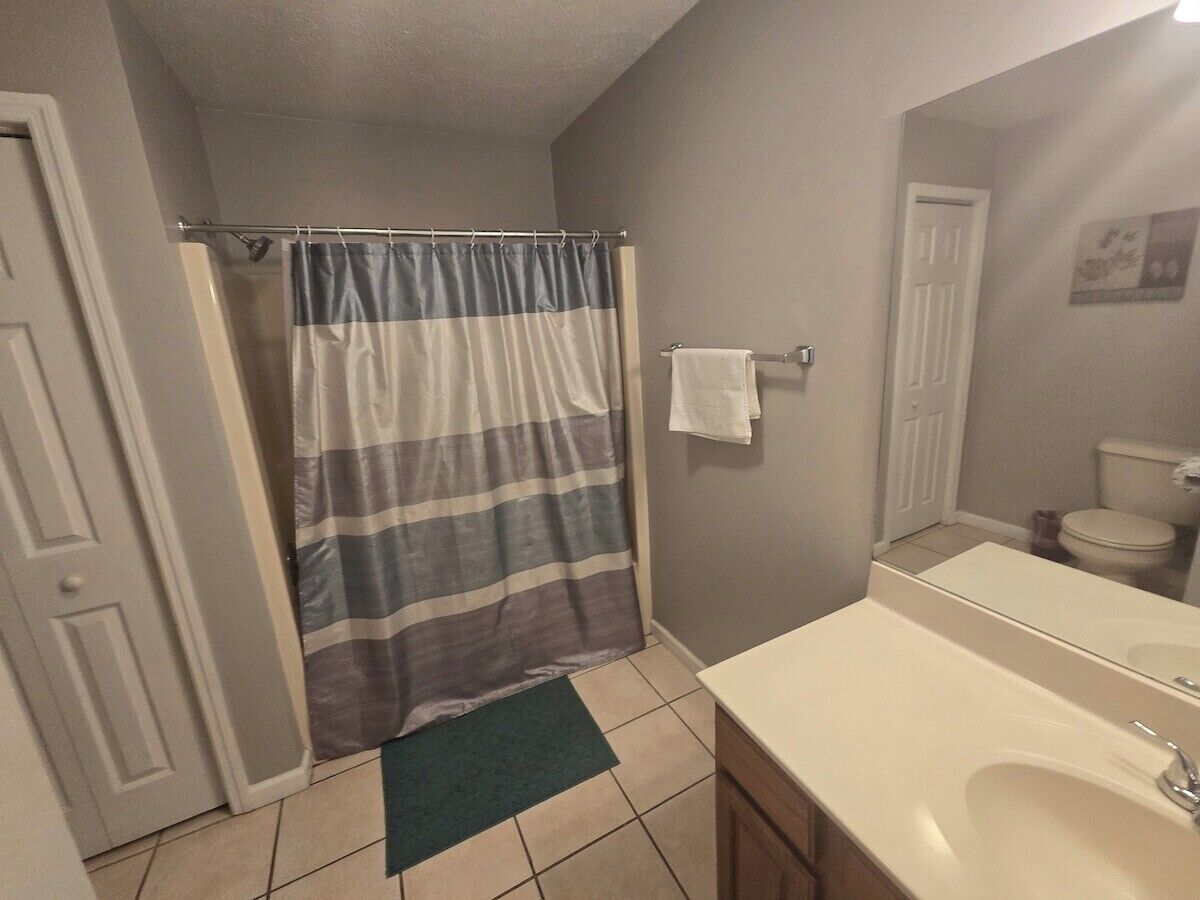 A bathroom with a shower curtain, a sink, a mirror, and a toilet.