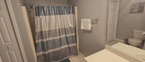 A bathroom with a shower curtain, a sink, a mirror, and a toilet.