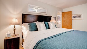A neatly made bed with a quilted blue blanket, a wooden headboard, and a bedside table with a lamp and a tissue box. - Cozy 2bd 2ba near Nob Hill home Garage Parking (Albuquerque)